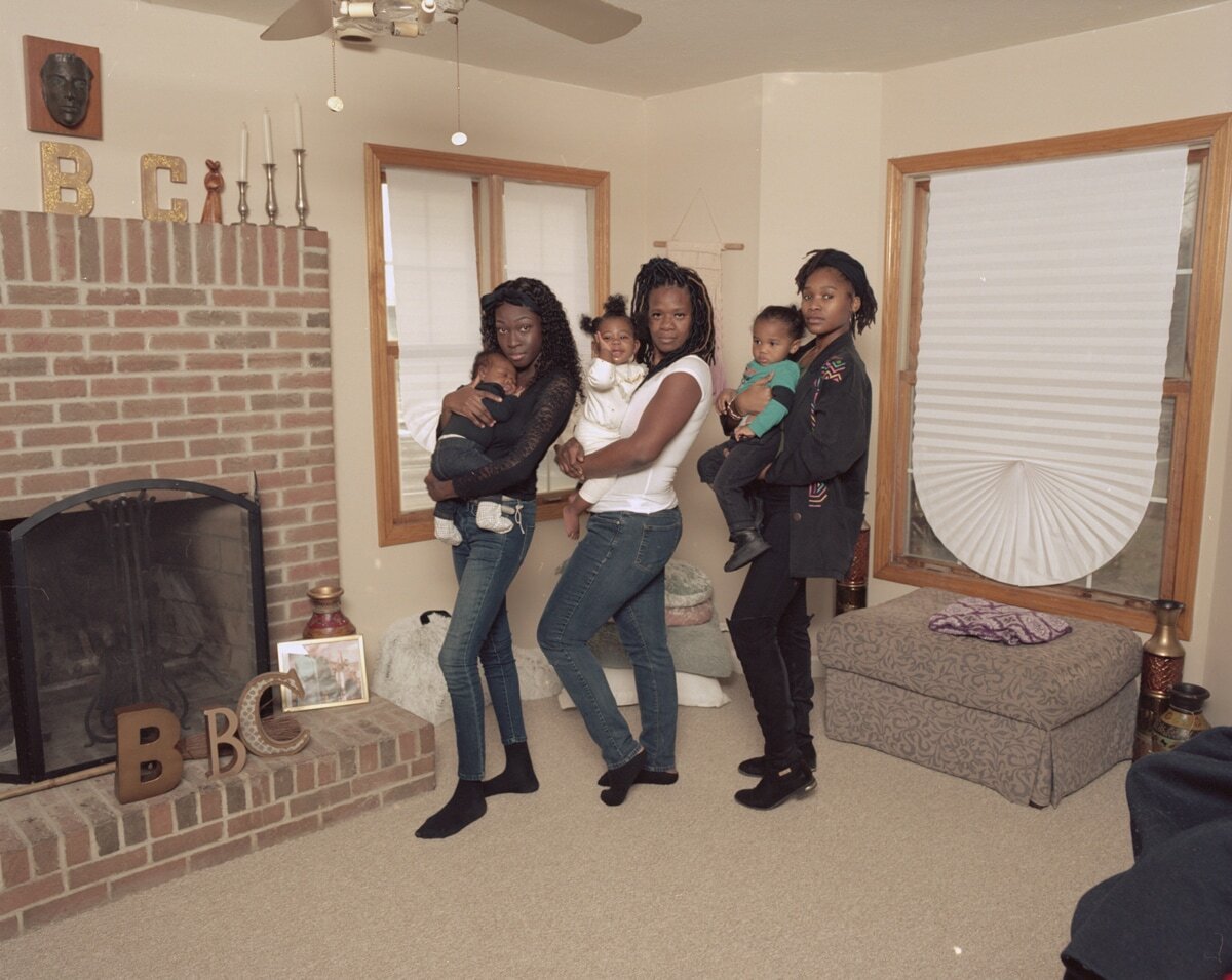 Color photograph by Deana Lawson of three women, each holding an infant, arranged in a line in a living room